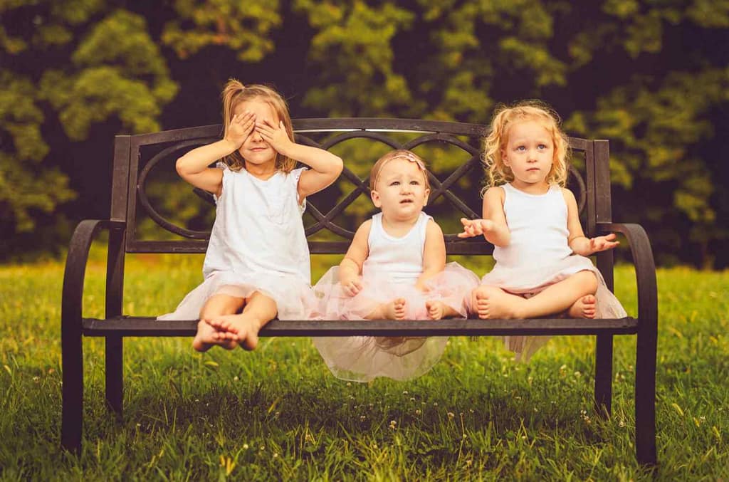 Three cute little girls on a park bench get their family pictures taken